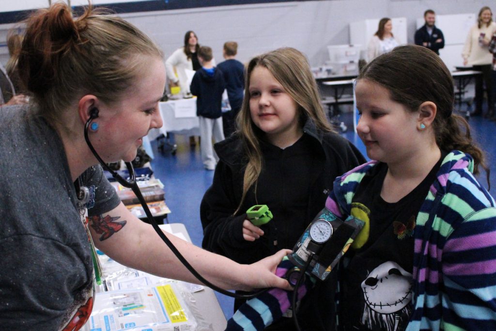 Pictured from left: WVU Reynolds Memorial Hospital ER RN Nikole Howearth shows Central Elementary third graders Kinley Ragland and Lilly Morgan how to take blood pressure and read a pulse.